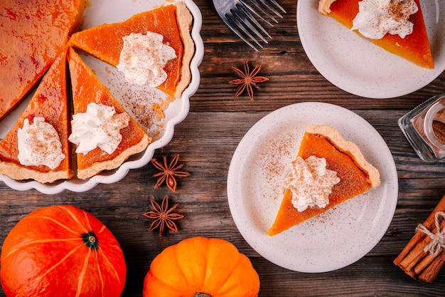 Tarte à la citrouille maison pour Thanksgiving avec de la crème fouettée et de la cannelle sur fond de bois