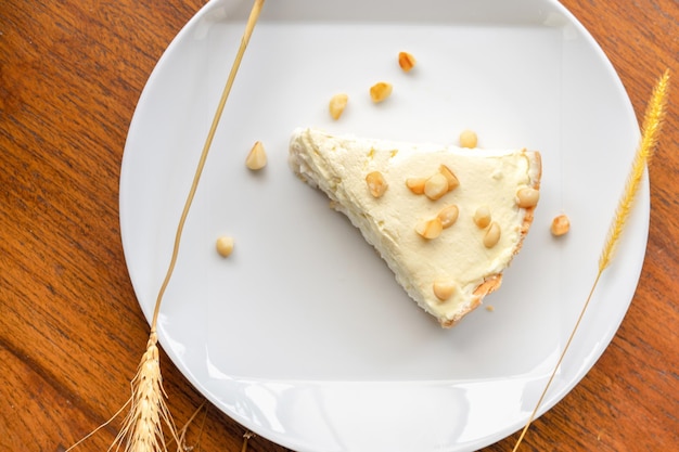 Tarte à la crème de noix de coco dans le plat blanc sur la table en bois qui garnit de macadamia Tournage au soleil