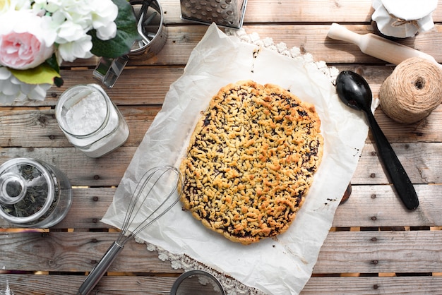 Tarte entière râpée sur une feuille de papier parchemin entouré d'ustensiles de cuisine sur une vue de dessus de table en bois