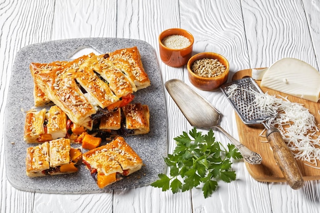 Tarte feuilletée aux légumes américaine avec fromage de chèvre garnie de graines de tournesol et de sésame remplie de légumes rôtis servie sur un fond en bois blanc, vue de dessus, gros plan