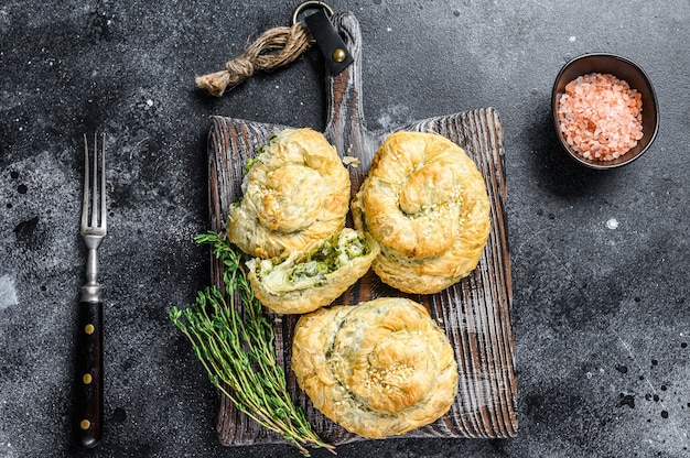 Tarte feuilletée en spirale Spanakopita cuite au four avec fromage feta et épinards. Fond noir. Vue de dessus.