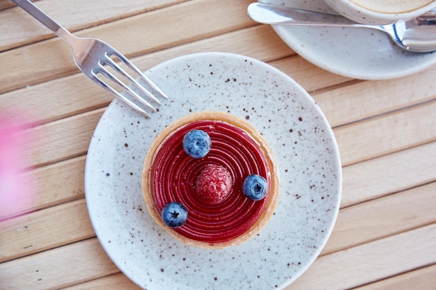 Tarte française aux myrtilles et aux framboises sur une assiette en céramique blanche avec une tasse de cappuccino Petit-déjeuner à l'heure du café Vue de dessus