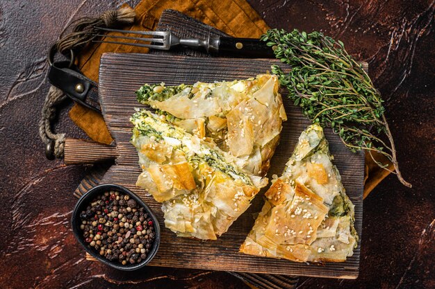 Tarte grecque Spanakopita aux épinards et fromage sur planche de bois. Fond sombre. Vue de dessus.