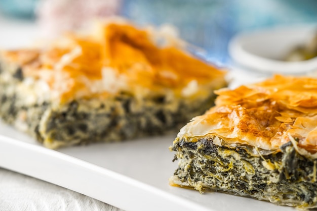 Tarte grecque spanakopita sur la plaque blanche avec des accessoires flous horizontaux