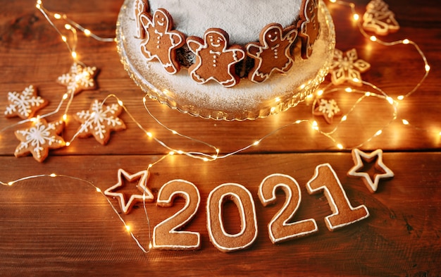 Tarte de Noël maison décorée de biscuits chiffres de personnes, sur la table en bois brun avec des nombres de nouvel an et de lumières