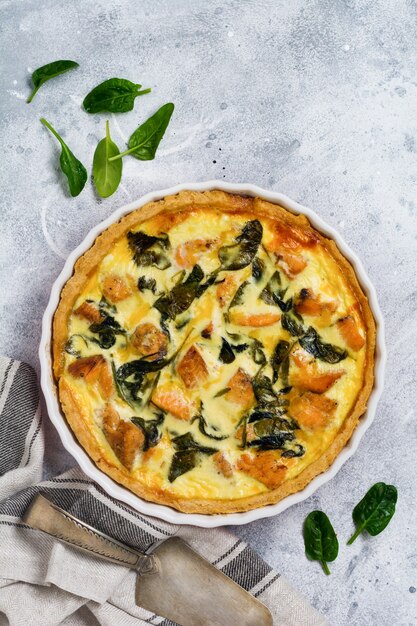 Tarte quiche maison au poisson rouge et aux épinards sur une surface en bois clair