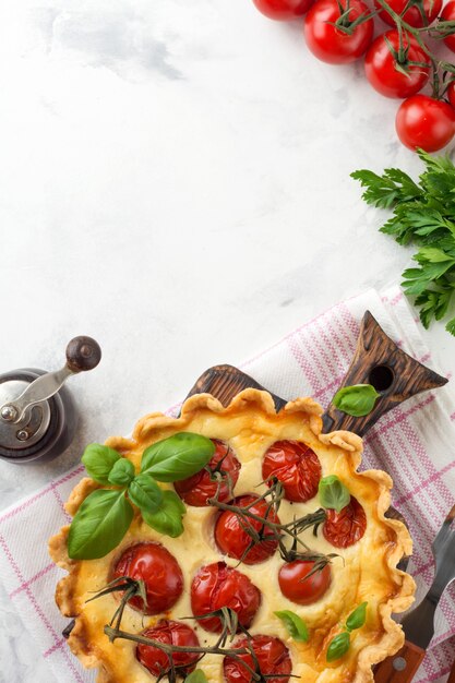 Tarte quiche maison aux tomates cerises, basilic, assaisonnements et fromage sur fond de pierre blanche. Mise au point sélective