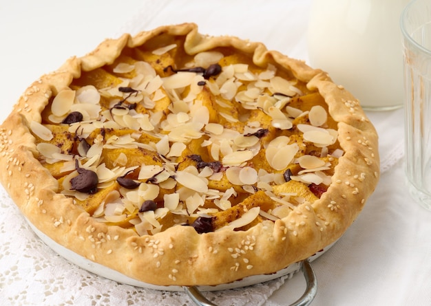 Tarte ronde cuite au four avec des morceaux de pomme, saupoudrée de flocons d'amandes sur une table blanche, vue de dessus