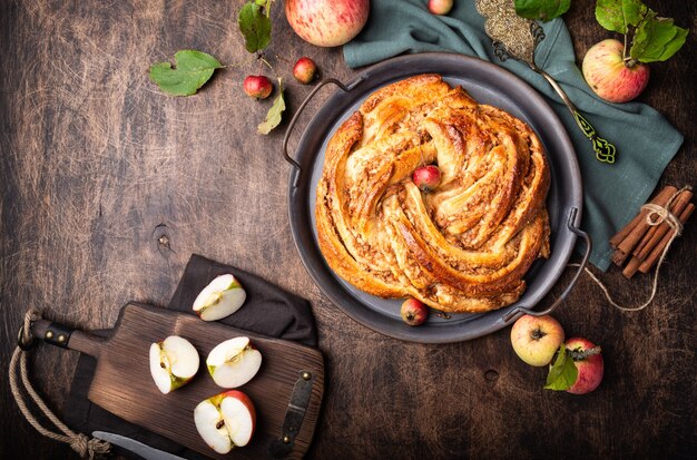 Tarte tordue maison fraîche avec garniture de pomme et de cannelle dans le bac vintage sur fond de contreplaqué rustique. Vue de dessus.