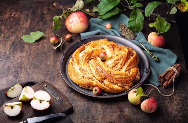 Tarte tordue maison fraîche avec garniture de pomme et de cannelle en plateau vintage sur contreplaqué rustique.