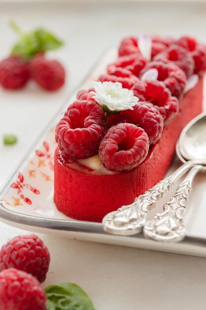 Tartelette de framboise décorée de fleurs sur une assiette avec des cuillères antiques Fond blanc