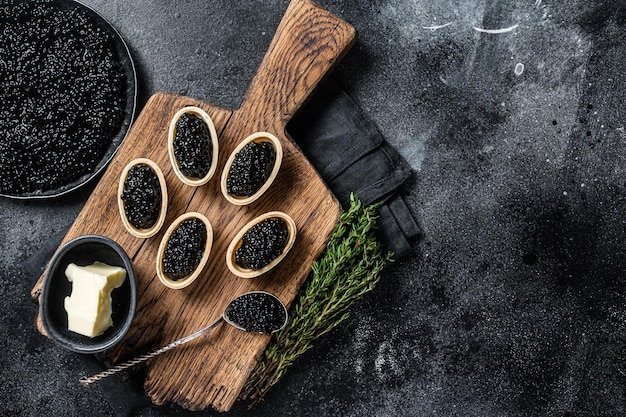 Tartelettes au caviar noir d'esturgeon sur planche de bois Fond noir Vue de dessus Espace de copie