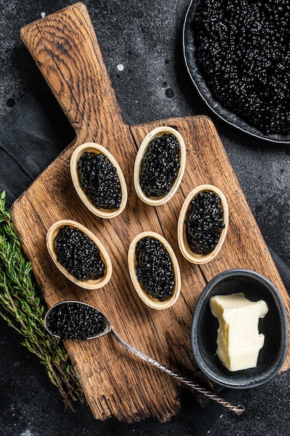 Tartelettes au caviar noir d'esturgeon sur planche de bois Fond noir Vue de dessus