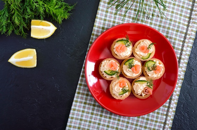 Tartelettes au fromage à la crème et saumon salé sur une assiette rouge. Collation légère et savoureuse pour une fête. Nourriture à manger avec les doigts. La vue de dessus.