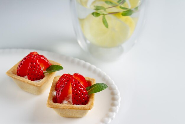 Tartelettes carrées avec des fraises au yogourt et des feuilles de menthe sur une assiette blanche et un verre d'eau avec un espace de copie au citron mise au point sélective