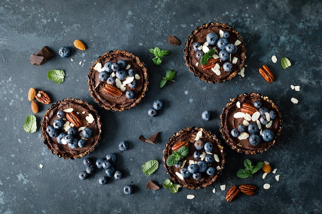 Tartelettes de dattes végétaliennes crues saines avec crème au chocolat de noix de cajou décorées de noix de pécan aux amandes et de myrtilles fraîches