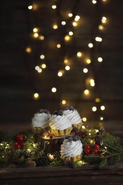 Tartelettes festives à la crème sur fond sombre avec sapin et lumières