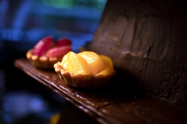 Photo tartelettes à la mangue jaune et à la fraise rouge sur une assiette de chocolat dans une boulangerie ou une pâtisserie