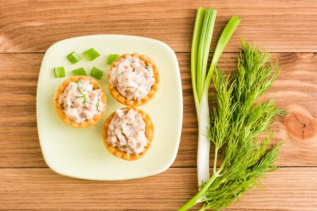 Tartelettes avec salade dans une soucoupe et légumes verts sur une table en bois