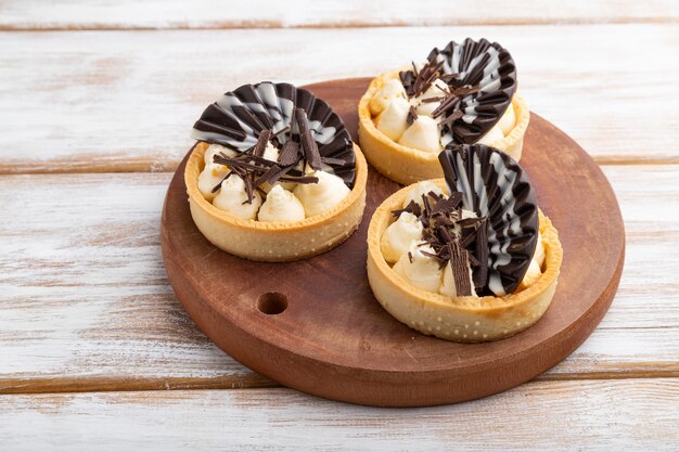 Tartelettes sucrées au chocolat et crème au fromage sur un fond en bois blanc. vue de côté, gros plan.