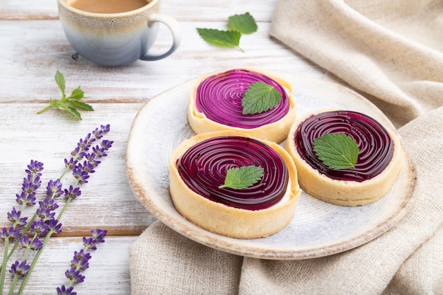 Tartelettes sucrées à la gelée et crème de lait avec tasse de café sur une surface en bois blanc et textile en lin