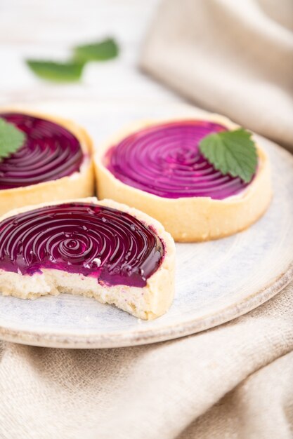 Tartelettes sucrées à la gelée et crème de lait avec tasse de café sur une surface en bois blanc et textile en lin