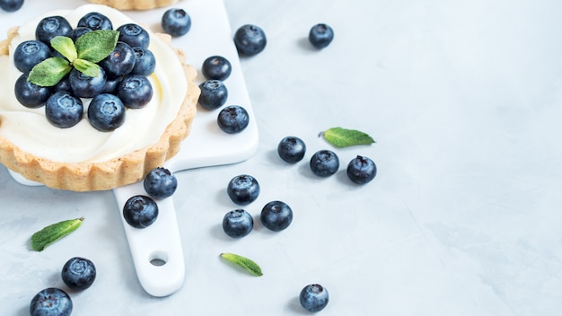 Tartelettes à la vanille avec baies de myrtille et feuilles de menthe sur fond clair