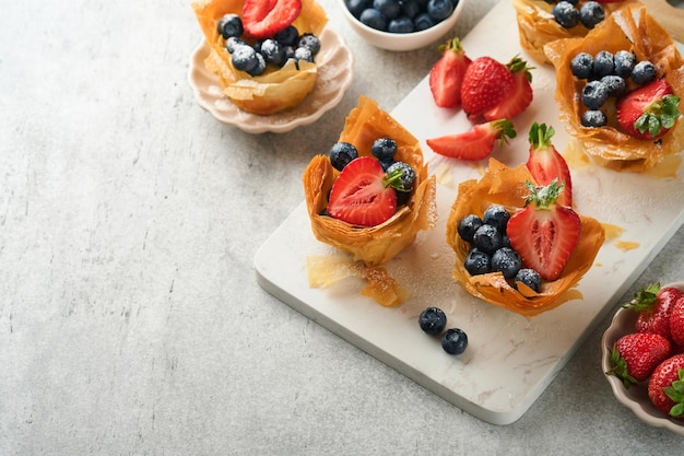 Tartes phyllo ou filo avec garniture au fromage aux fraises et aux myrtilles aux baies fraîches garnie de menthe fraîche sur une assiette blanche Paskets de pâtisserie filo maison Délicieux dessert de pâtisserie filo