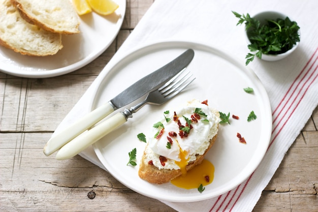 Tartines croustillantes à la baguette avec fromage cottage, œuf poché et tomates séchées sur fond clair.