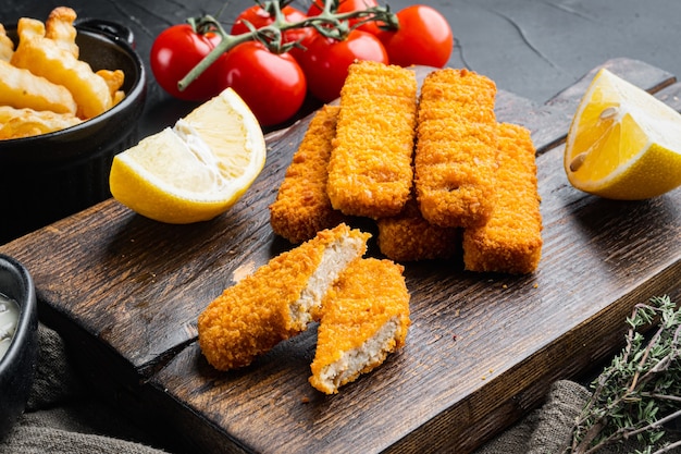 Tas de bâtonnets de poisson frits dorés avec sauce à l'ail blanc, sur une planche à découper en bois, sur fond noir