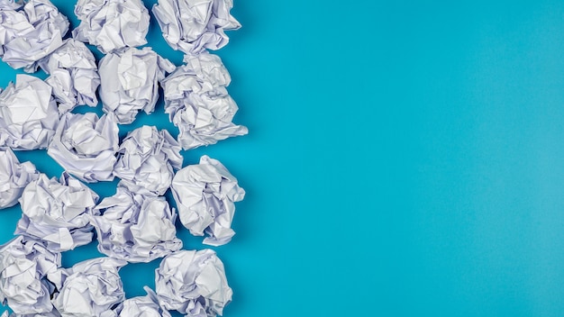 Tas de boules de papier froissé blanc sur fond bleu.