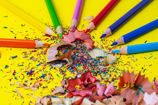 Tas de copeaux multicolores et crayons de couleur sur un gros plan de table jaune vif