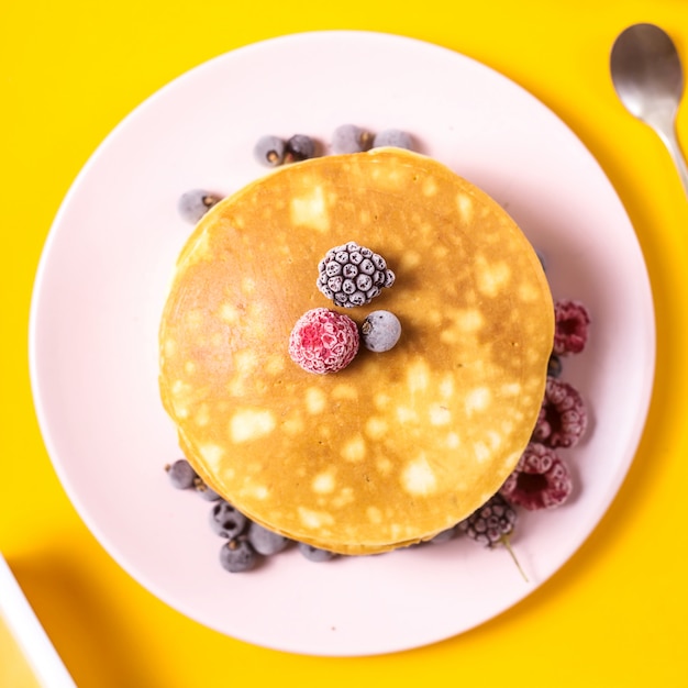 Tas de crêpes sur une assiette rose avec des mûres, des framboises et des mûres