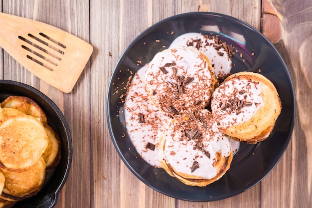 Un tas de crêpes fourrées au yaourt aux fruits et saupoudrées de chocolat râpé sur une assiette sur une table en bois