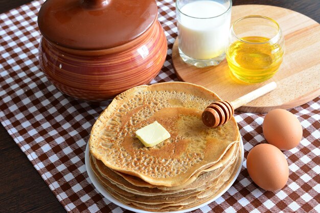 tas de crêpes frites chaudes sur une assiette sur une table rustique avec nappe, miel, pot en céramique et œufs