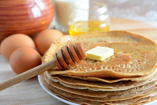 tas de crêpes isolées sur une assiette avec un morceau de beurre, une louche de miel et des œufs, macro