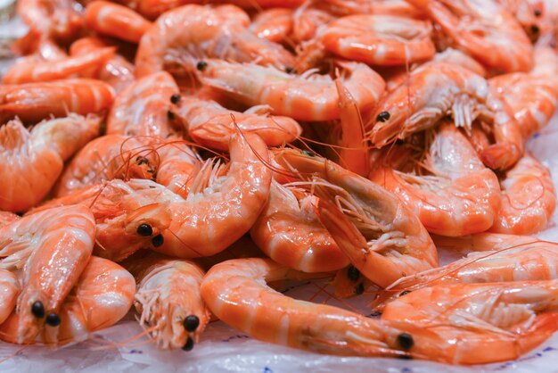 Un tas de crevettes orange crues se trouve sur la glace froide du comptoir du réfrigérateur du marché alimentaire délicieux