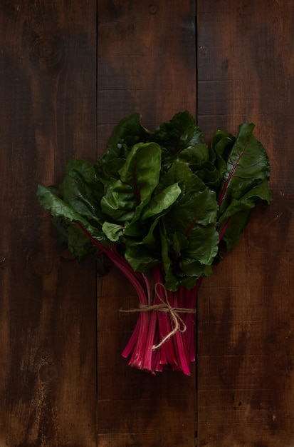 Un tas de feuilles vertes de bette à carde fraîche avec des tiges rouges attachées avec de la ficelle sur une table en bois sombre V