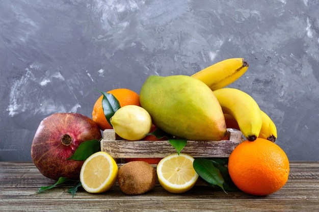 Un tas de fruits exotiques (bananes, oranges, kiwi, grenade, mangue, goyave, citron) dans une boîte en bois sur la table.