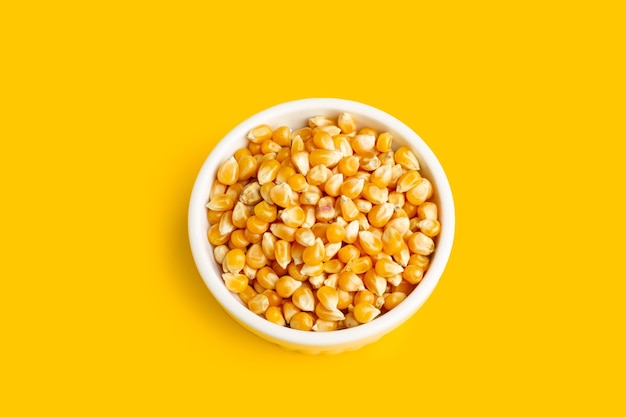 Un tas de grains de maïs dans un bol en céramique blanche sur fond jaune avec espace de copie