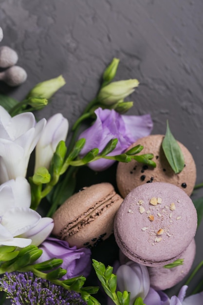 Tas de macarons français sucrés mélangés à des fleurs sur fond de béton gris