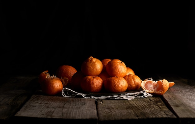 Tas de mandarine orange mûre ronde non pelée dans une assiette sur une surface noire