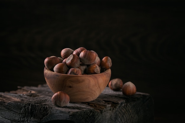 Tas de noisettes filbert dans un bol en bois sur une surface en bois sombre. Noix fraîches dans leurs coquilles.