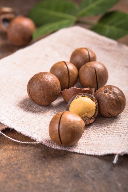 Tas de noix de macadamia avec coquilles dans un sac sur la table en bois