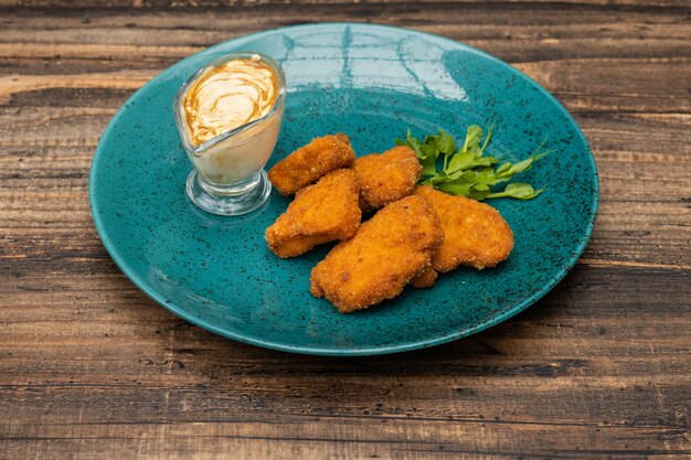 Un tas de nuggets de poulet sur plaque bleue avec sauce et vert