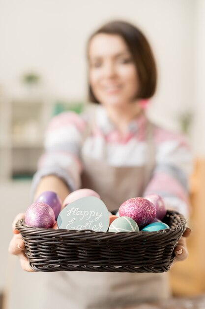 Tas d'oeufs de Pâques peints colorés et petite carte de voeux dans le panier tenu par jeune femme décontractée