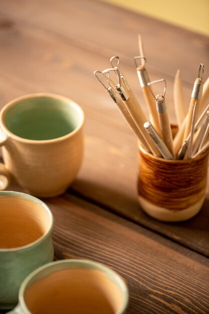 Tas d'outils à main spéciaux pour travailler avec de l'argile et faire de la terre cuite sur table en bois avec groupe de tasses à proximité