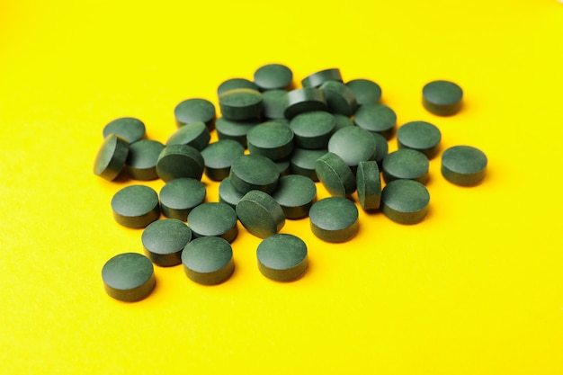 Tas de pilules de spiruline sur fond jaune, gros plan