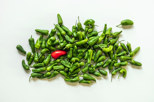 Un tas de poivrons padron verts et un rouge solitaire sur une surface blanche lisse