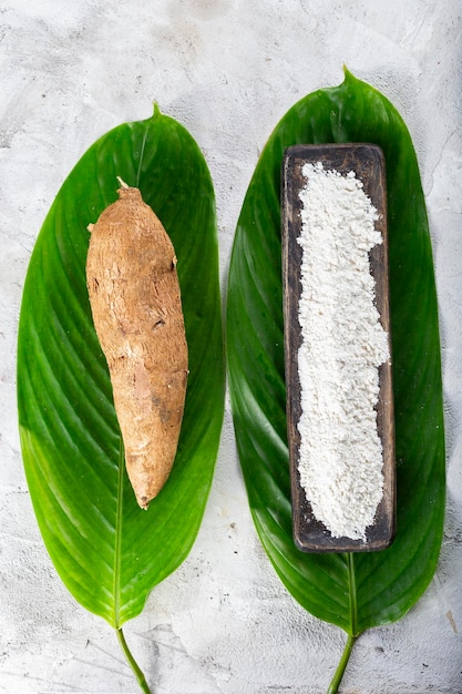 Tas de racine de manioc et de farine de manioc sur un fond texturé gris et blanc Manihot esculenta